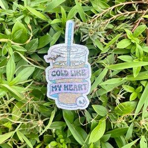 Pu&ograve; includere: Un adesivo scintillante di una bevanda fredda con una cannuccia e un teschio. L'adesivo ha il testo "Cold Like My Heart".