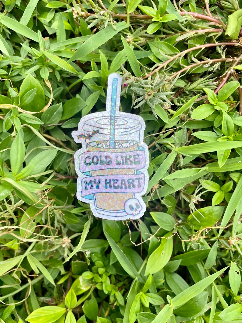 Pu&ograve; includere: Un adesivo scintillante di una bevanda fredda con una cannuccia e un teschio. L'adesivo ha il testo "Cold Like My Heart".