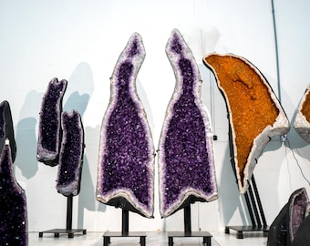 Könnte beinhalten: Eine Sammlung großer Amethyst- und Citrin-Geoden, die auf schwarzen Metallständern ausgestellt sind. Die Geoden sind aufgeschnitten, um die Kristalle im Inneren zu zeigen.