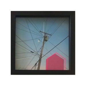 May include: A framed photograph of a power pole with a lightbulb at the top, surrounded by a network of wires against a blue sky. A bright pink geometric shape is partially visible in the lower right corner of the image.