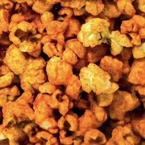 May include: Close-up of seasoned popcorn kernels. The popcorn is coated in a vibrant orange seasoning, with visible spices and herbs. The image showcases a textured, appetizing snack, perfect for movie nights or casual gatherings.