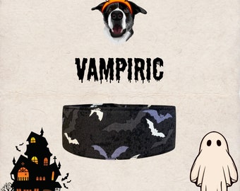 May include: A black and white dog wearing a black and grey patterned dog collar with a black and white bat design. The dog is wearing a headband with two orange pumpkins on top. The text "VAMPIRIC" is written in black dripping letters. A white ghost and a black silhouette of a haunted house are in the background.