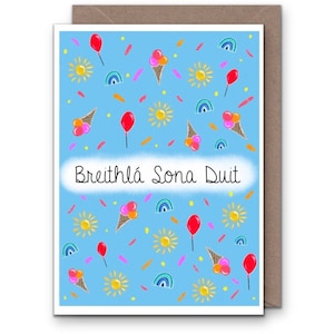 May include: A blue card with a happy birthday message in Irish, "Breithla sona duit." The card is decorated with a pattern of red balloons, yellow suns, ice cream cones, and rainbows.