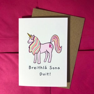May include: A white card featuring a pink unicorn with a rainbow mane and tail. The card reads "Breithla Sona Duit!" which is Irish for "Happy Birthday to You!"