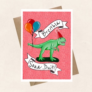 May include: A pink card featuring a green dinosaur wearing a red party hat and holding balloons. The card reads "Breithla sona duit!" which is Irish for "Happy birthday!"