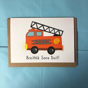 May include: A red fire engine with a yellow ladder and a yellow spiral on the side. The engine has black wheels and a yellow light on the front. The text "Breithla Sona Duit!" is written below the engine.