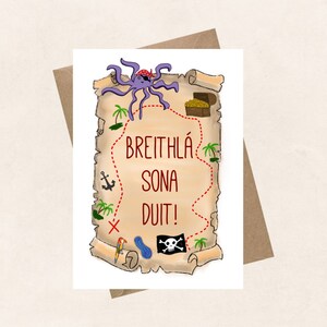 May include: A light brown, rolled-up parchment paper with a red line drawn around it. The parchment paper has a purple octopus with a pirate hat on top of it. The parchment paper has a red anchor, a red X, a blue pool, a pirate skull and crossbones, and a parrot with a blue and yellow body. The parchment paper has the text "BREITHLA SONA DUIT!" in red.