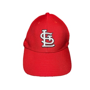 May include: A bright red baseball cap featuring the white and black embroidered letters STL intertwined on the front center. The cap has a structured crown, a curved brim, and small ventilation eyelets at the top of each panel of the fabric.