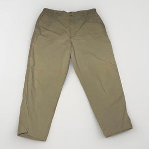 May include: A pair of solid khaki-colored trousers featuring an elasticized waistband, a central button closure, and a fly front. These pants have a relaxed fit with straight legs and side pockets, constructed from a plain, matte-finish fabric.