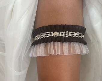 Liga de novia confeccionada en satén negro y organza blanca con detalle de lazo en tonos de diamantes de imitación