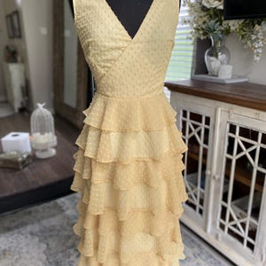 A photo of the sample dress on a mannequin showing the full front of the dress. It has a faux wrap neckline and is sleeveless. The skirt has evenly spaced rufled tiered layers creating a romantic and sassy vibe.