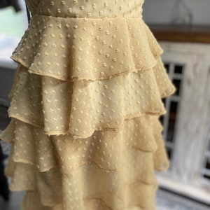 A photo of the sample dress on a mannequin showing a close up on the skirt layers. The fabric used is a clip spot with a chiffon base. It is a beautiful sunflower yellow color and has little rectangular spots. The rectangular spots are raised and have texture like a pile. The skirt layers are all the same length and have a nice flow to bottom while not having any gathers at the top.