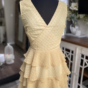 A photo of the sample dress on a mannequin showing the front bodice of the dress. It has a faux wrap neckline and is sleeveless.You can see the top of the skirt. The skirt has evenly spaced rufled tiered layers creating a romantic and sassy vibe.