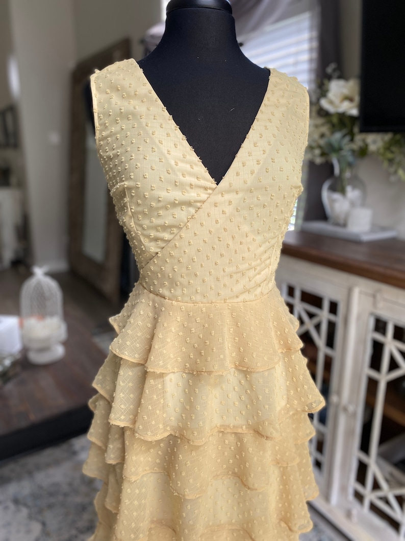 A photo of the sample dress on a mannequin showing the front bodice of the dress. It has a faux wrap neckline and is sleeveless.You can see the top of the skirt. The skirt has evenly spaced rufled tiered layers creating a romantic and sassy vibe.