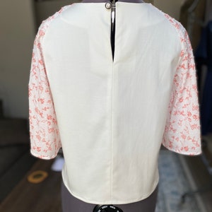 A photo of the sample top on a mannequin showing the full back. The back is full coverage with a high scoop neckline and raglan sleeves. There is a keyhole opening at the top of the centerback with a button closure so you can get into the top.