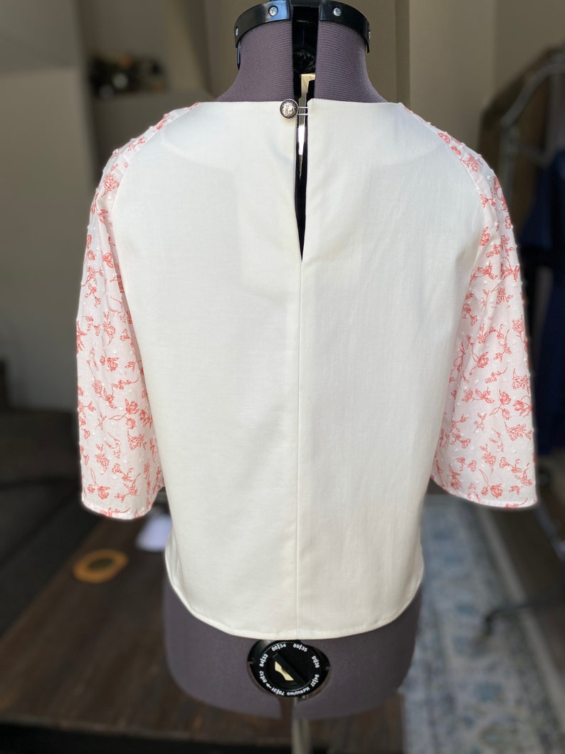 A photo of the sample top on a mannequin showing the full back. The back is full coverage with a high scoop neckline and raglan sleeves. There is a keyhole opening at the top of the centerback with a button closure so you can get into the top.
