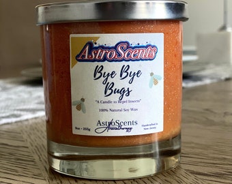 May include: A glass jar candle with a silver lid. The candle is orange and has glitter in it. The label says "Astro Scents Bye Bye Bugs" and "A Candle to Repel Insects". It also says "100% Natural Soy Wax" and "Astro Scents Aromatherapy".