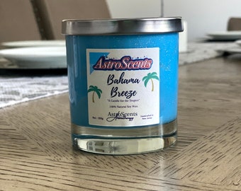 May include: A blue soy wax candle in a clear glass jar with a silver lid. The label reads AstroScents Bahama Breeze, A Candle for the Tropics, 100% Natural Soy Wax, 9oz 255g, Handcrafted in New Jersey, featuring two green palm tree illustrations.