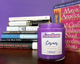 May include: Purple candle with a glittery finish and a label that reads "Astro Scents Cosmos A Candle for Meditation 100% Natural Soy Wax Astro Scents Aromatherapy Handmade in New Jersey".