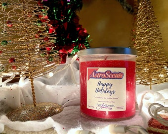May include: A red candle with glitter in a glass jar with a silver lid. The candle has a label that says "AstroScents Happy Holidays" and "A Candle for the Holiday Season". The candle is surrounded by gold wire Christmas trees and white lights.