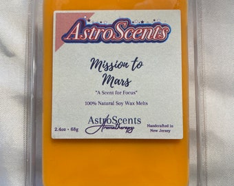 May include: A 2.4 ounce, 68 gram soy wax melt in a clear plastic container. The wax melt is orange and has the text "Astro Scents Mission to Mars "A Scent for Focus" 100% Natural Soy Wax Melts AstroScents Aromatherapy Handcrafted in New Jersey" printed on the label.