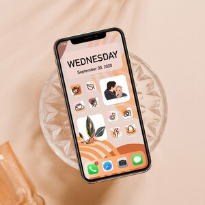 May include: A gold iPhone with a custom home screen featuring a Wednesday date, September 30, 2020, and icons for various apps, including Instagram, TikTok, Facebook, Snapchat, and a calendar app. The phone is on a clear glass coaster with a brown background.