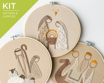 May include: Three embroidery hoop art pieces featuring Nativity scenes. Each hoop has a beige fabric background with detailed thread work in brown, beige, and white. One depicts the Holy Family, another the shepherds, and the third the Three Wise Men.