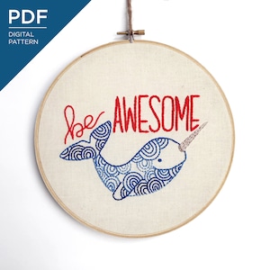 May include: Embroidered narwhal hoop art with the words "be AWESOME" in red thread. The narwhal is blue with a patterned design. The hoop is made of wood and the fabric is a light beige color. A digital pattern is available.