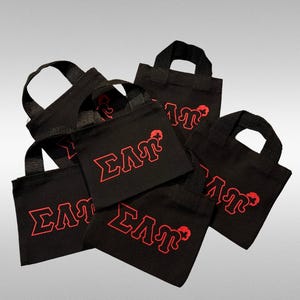 Op de afbeelding: Een stapel van zes zwarte draagtassen met rode letters die "ΣΛΠ" op elke tas zeggen.