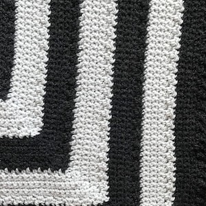 May include: Black and white striped crocheted blanket with a geometric pattern. The blanket is made with a soft, fluffy yarn.