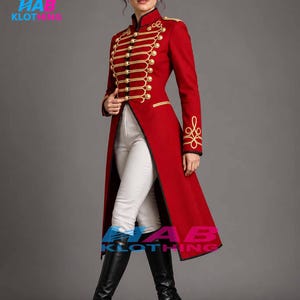 May include: A long red military-style coat featuring gold braided cord detailing, gold buttons, and black trim. The coat is paired with white trousers and black knee-high boots. The HAB KLOTHING logo is visible in the top left and bottom center.