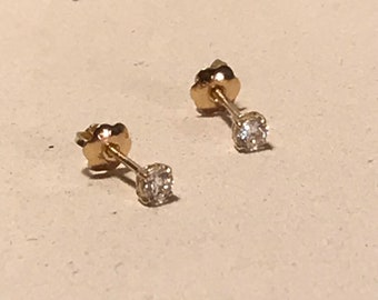 May include: A pair of gold stud earrings with small, clear gemstones.