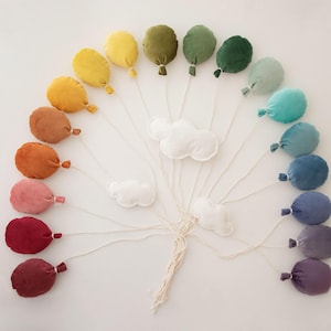 May include: A rainbow of felt balloons with white felt clouds hanging from strings. The balloons are arranged in a semi-circle with the clouds in the centre.