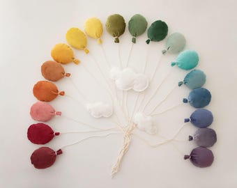 May include: A rainbow of felt balloons with white felt clouds hanging from strings. The balloons are arranged in a semi-circle with the clouds in the center.