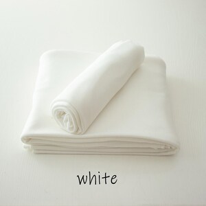 May include: A solid white fabric textile folded into a stack with a single rolled piece resting on top. The word white is printed in black lowercase letters below the fabric, indicating the color of the material shown in the image.
