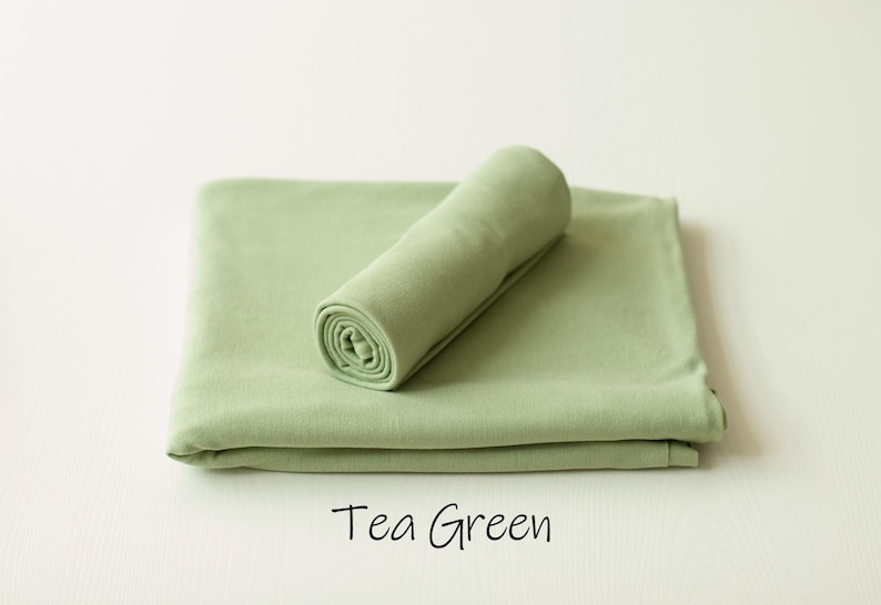 May include: A tea green fabric wrap featuring a smooth, solid-colored textile surface. The item consists of one piece folded flat into a rectangular shape with a second piece rolled into a cylinder and placed on top. The text Tea Green is visible.