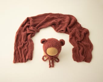 May include: A rust-colored knitted baby hat with bear ears and a matching wrap. The hat and wrap are made of a soft, fuzzy material.