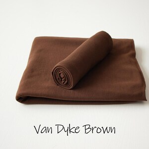 May include: A solid dark brown fabric piece folded into a rectangular shape with a smaller, tightly rolled section of the same material resting on top. The text Van Dyke Brown is printed in a simple black font below the fabric.