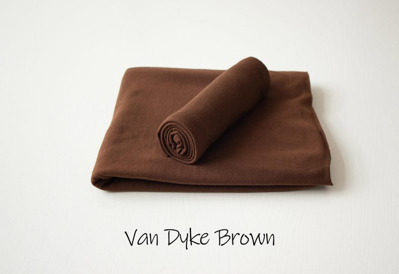May include: A solid dark brown fabric piece folded into a rectangular shape with a smaller, tightly rolled section of the same material resting on top. The text Van Dyke Brown is printed in a simple black font below the fabric.