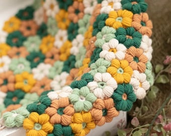 May include: A crocheted blanket with a floral pattern in shades of green, yellow, and orange. The blanket is made of soft yarn and has a textured surface.