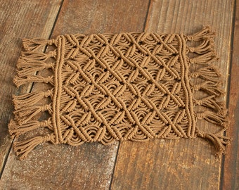 May include: A brown macrame rug with fringe on all sides. The rug is made with a diamond pattern and has a natural, earthy look.