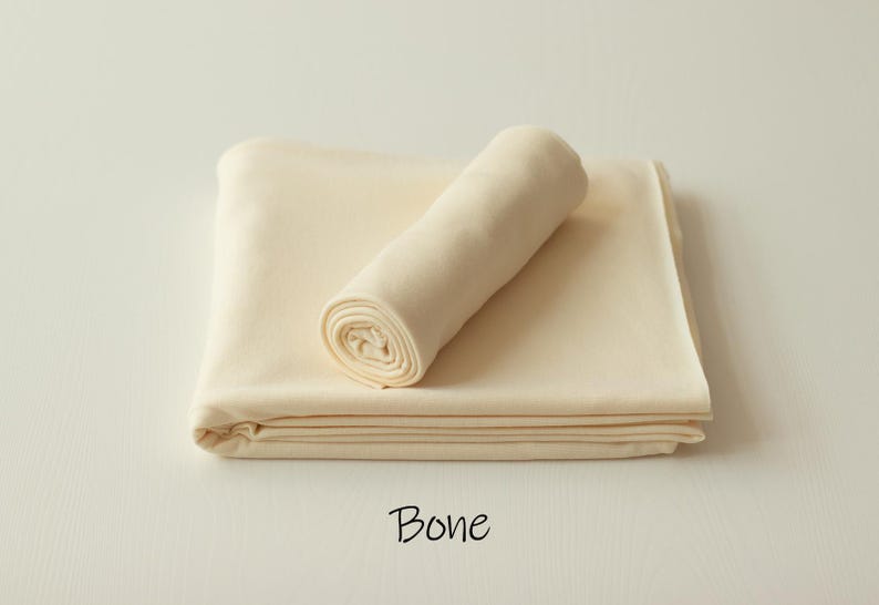May include: A folded piece of solid bone-colored fabric with a smooth texture, featuring a rolled section resting on top of the flat base. The word Bone is printed in black text below the fabric, indicating the specific color of the material.