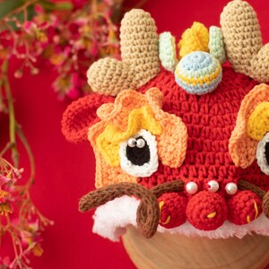 May include: A red, orange and yellow crocheted lion dance hat with white fur trim and pearl-like beads. The hat has a small, multi-coloured ball on top.