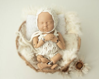 May include: A white crocheted baby doll with a white crocheted hat, lying in a brown wicker basket lined with white faux fur. The doll is wearing a white crocheted dress.