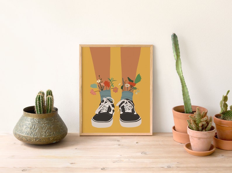 May include: A framed illustration of a pair of black trainers with flowers growing out of the tops. The background is a yellow colour.