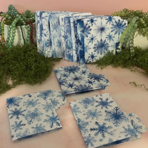 May include: A collection of small, rectangular paper folders featuring a blue and white snowflake pattern. The folders are arranged in a row in the background, with three additional folders placed in the foreground, each showing a tab on the side.