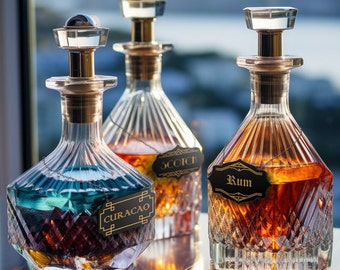May include: Three decorative glass bottles with stoppers and labels. The bottles are filled with different colored liquids. The labels read "Scotch", "Rum", and "Curacao".