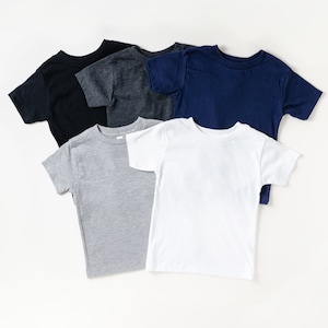 May include: Five short-sleeved t-shirts in various colors: black, charcoal gray, navy blue, light gray, and white. The shirts are arranged in a layered, overlapping pattern, showcasing the different hues and styles.