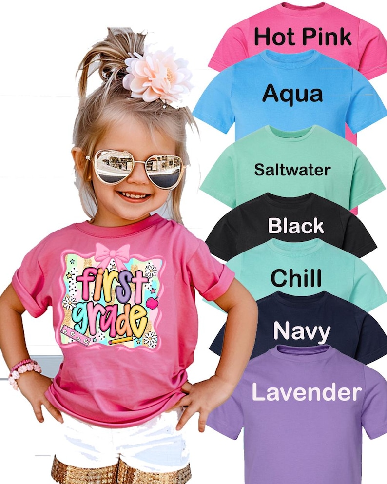 May include: A young girl wearing a pink t-shirt with the words "First Grade" in a colorful design. The image also shows examples of t-shirts in various colors, including hot pink, aqua, saltwater, black, chill, navy, and lavender.