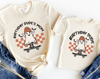 May include: Two cream-colored t-shirts with a ghost skateboarding graphic. The larger shirt says "Birthday Dude's Mom" and the smaller shirt says "Birthday Dude".